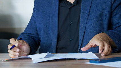 An adult man in a business suit, sitting at a table with a pen, fills out an agreement or order...