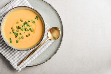 Pumpkin soup in a bowl with pumpkin seeds, green onions and breadsticks - obrazy, fototapety, plakaty