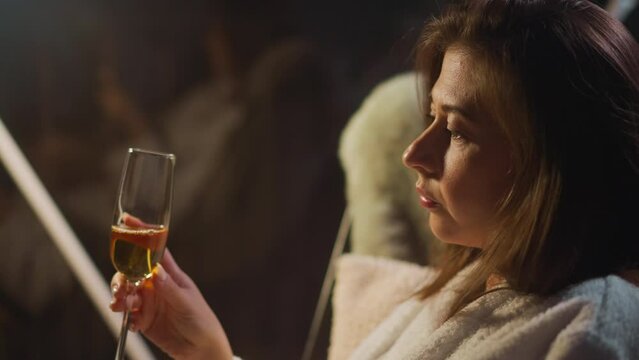 Sad lady drinks alcohol to muffle moral pain sitting near window with reflection. Female dealing with mental problem that makes feel depressive and alone slow motion