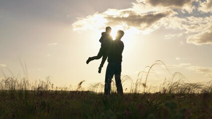 Silhouette, father child son, play together in park in front of sun. Dad plays with his son, throws child up into sky with his hands, happy child smiles. Concept of family happiness. Child is flying