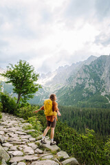 Naklejka premium Young traveler woman with a yellow backpack on a cliff enjoying mountain views. Sports concept, traveler. Active lifestyle.