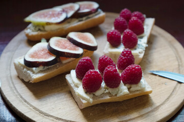 Baguette with blue cheese, figs and raspberries on wooden cutting board