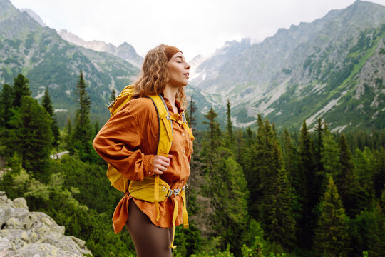 Young traveler woman with a yellow backpack on a cliff enjoying mountain views. Sports concept, traveler. Active lifestyle.