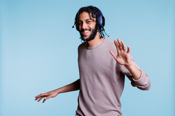 Happy arab man in earphones enjoying dance party while listening to music and looking at camera....