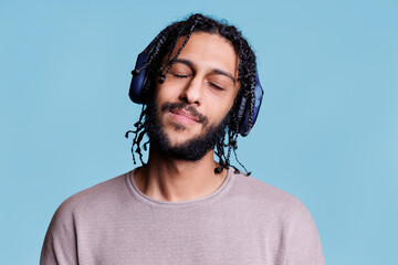Relaxed arab man enjoying music wearing wireless headphones with closed eyes. Handsome young model...