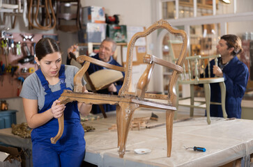Young female furniture maker working on vintage chair in workshop - obrazy, fototapety, plakaty