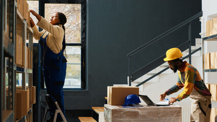 Team of warehouse employees taking boxes from racks, woman climbing ladder and men using laptop for stock distribution. Group of workers preparing merchandise and packing supplies. © DC Studio