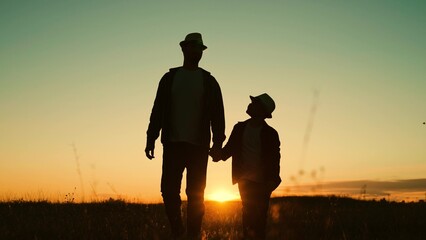 Kid dad travel to sunset, happy family. Silhouette. Father and son walk together holding hands in park at sunset. Dad plays with his kid outdoors in park. Childhood dream, fatherly. Child adolescence - obrazy, fototapety, plakaty