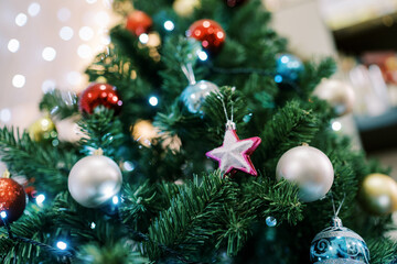Pink star next to silver and blue balls hangs on a Christmas tree
