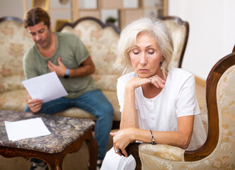 Mature couple fighting over papers at home, older woman ignoring man