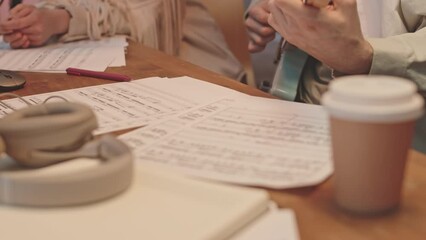 Zoom out close up shot of man playing guitar while sitting with girlfriend or music teacher at desk with sheet music on it