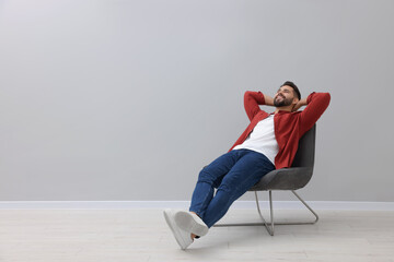 Handsome man relaxing in armchair near light grey wall indoors, space for text