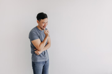 Evil looks of asian man in blue t-shirt smile and smirk stand isolated on white. - obrazy, fototapety, plakaty