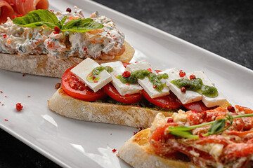 Bruschetta with homon, vegetables and cheese on a plate, on a gray concrete background