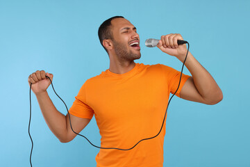 Handsome man with microphone singing on light blue background