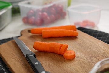 Wooden board with carrots, knife and containers on table, closeup. Food storage