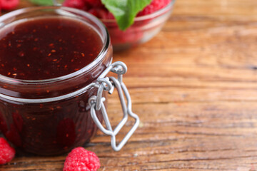 Jar of delicious raspberry jam and fresh berries on wooden table, closeup. Space for text