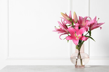 Beautiful pink lily flowers in vase on light grey table against white wall, space for text