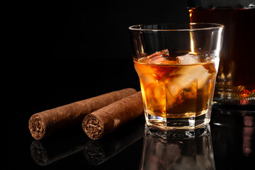 Glass of whiskey with ice cubes and cigars on black mirror surface, closeup