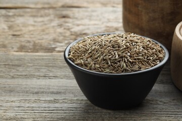 Bowl of caraway seeds on wooden table, closeup. Space for text