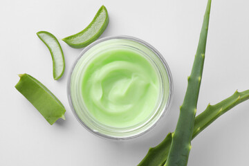 Jar of cosmetic cream and cut aloe leaves on white background, flat lay