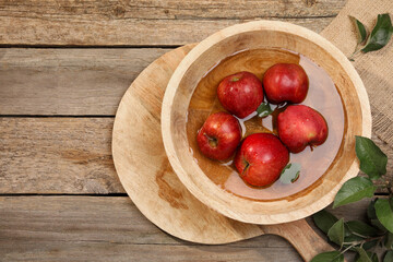 Fresh red apples in bowl with water and leaves on wooden table, flat lay. Space for text