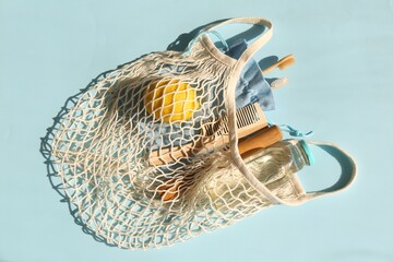 Fishnet bag with different items on light blue background, top view. Conscious consumption