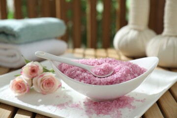 Bowl of pink sea salt and beautiful roses on wooden table, closeup
