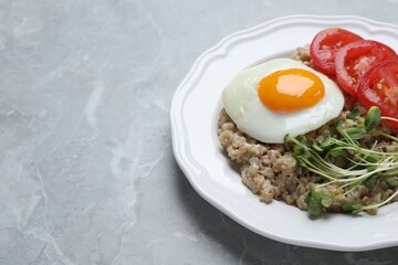 Delicious boiled oatmeal with fried egg, tomato and microgreens on light grey marble table, closeup. Space for text