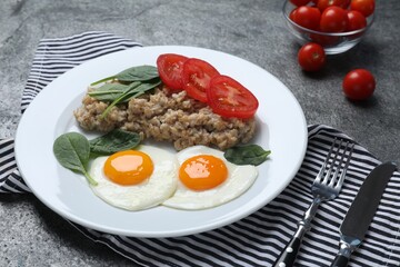 Delicious boiled oatmeal with fried eggs, tomato and basil served on grey table
