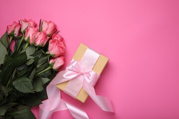 Gift box and beautiful flowers on pink background, flat lay. Space for text