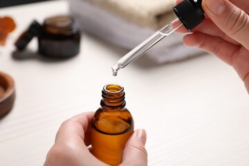 Woman with bottle of cosmetic serum and pipette at white table, closeup