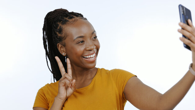 Black woman, peace sign and selfie for social media, influencer content creation or blog in studio. Happy young person with smile and emoji for profile picture or photography on a white background