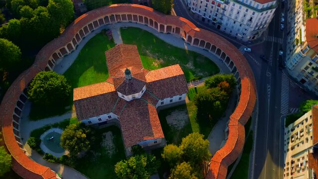 Aerial view of the Rotunda della Besana. Blue sky. Historical buildings in the city. A cruciform church surrounded by a wall. Cinematic filming using FPV drone. Tiled roofs. architecture Milan Italy