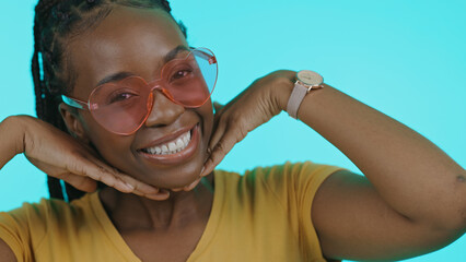 Happy, heart and portrait of a black woman with sunglasses for summer on a blue background. Smile, perfect and a model or African girl with trendy eyewear, fashion and hands on face on a backdrop
