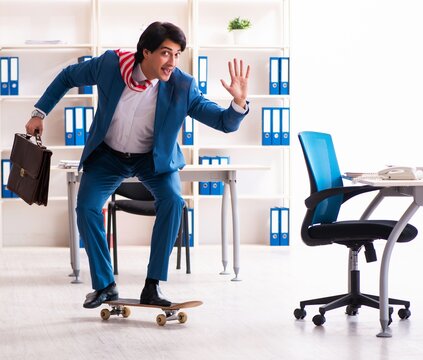 Young handsome businessman with longboard in the office