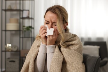 Sick woman wrapped in blanket blowing nose in tissue at home. Cold symptoms - obrazy, fototapety, plakaty