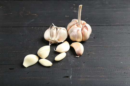 Several cloves of garlic placed on a black rustic wooden board.