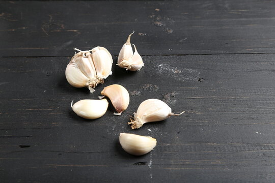 Several cloves of garlic placed on a black rustic wooden board.
