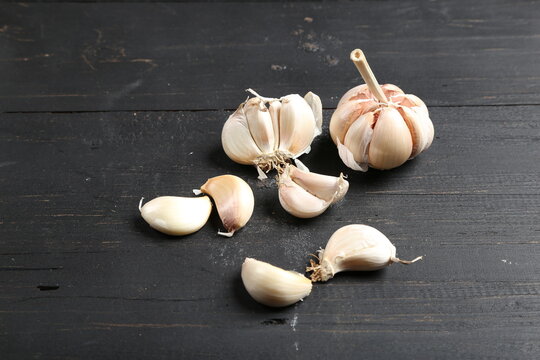 Several cloves of garlic placed on a black rustic wooden board.