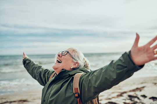 A senior woman with outstretched arms embracing the sea breeze on the beach