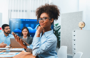 Happy young african businesswoman wearing glasses portrait with group of office worker on meeting with screen display business dashboard in background. Confident office lady at team meeting. Concord