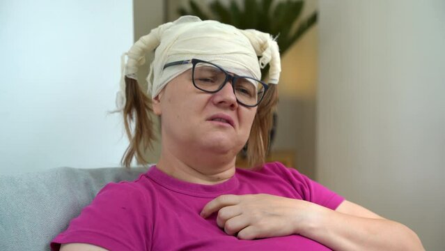 Woman in glasses with bandaged head holds heart with hand, shakes head in resignation, suffers from pain, complains about problems Pessimist mother-in-law talks about bad luck, patient psychotherapy