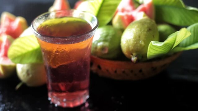 Cinematic shot of raw guava fruit cut in a stylish manner on a black wooden surface along with its extracted water in a glass alongside it. HD dolly shot. High-quality food fruit stock footage. 