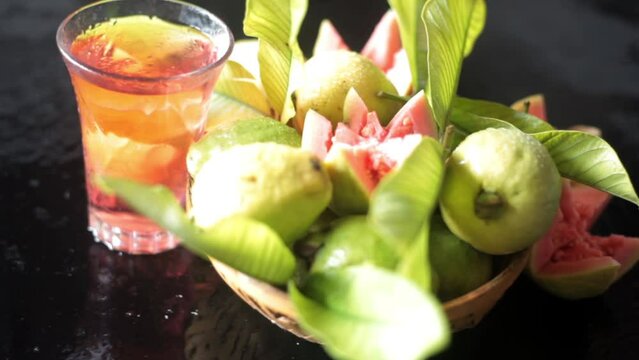 Cinematic shot of raw guava fruit cut in a stylish manner on a black wooden surface along with its extracted water in a glass alongside it. HD dolly shot. High-quality food fruit stock footage. 
