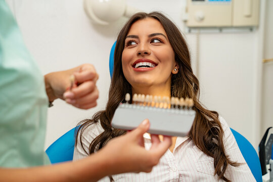 Amazing beautiful young woman sitting in dental chair, dentist holding teeth shade guide 