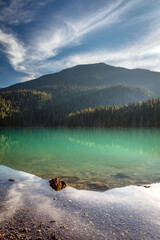 A dreamy reflection with sunlight on the mountains and turquoise water of Cheakamus Lake in Whistler, BC, Canada.
