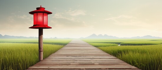 A wooden post and a classic red lantern stand together with a wooden pathway in a rice field scenery