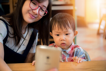 A young asian mother makes selfie with her little cute son at a table in a cafe