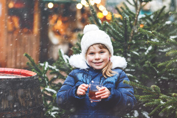 Little cute preschool girl drinking hot children punch or chocolate on German Christmas market. Happy child on traditional family market in Germany, Laughing boy in colorful winter clothes